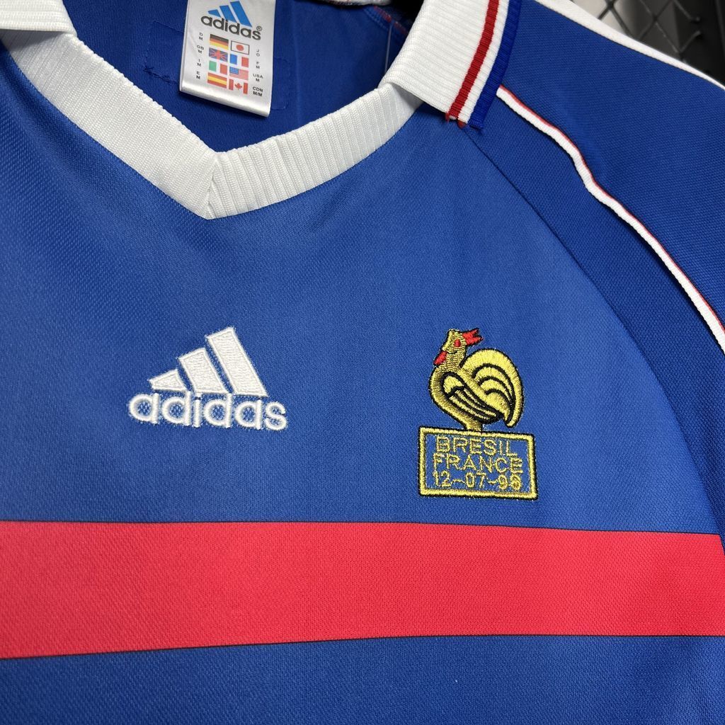 Blue football jersey close-up: Adidas logo and France crest over a red horizontal band.