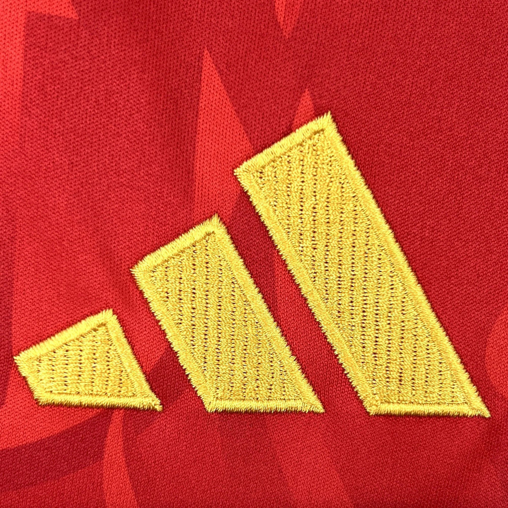 Red jersey fabric detail with three yellow Adidas logo stripes embroidery