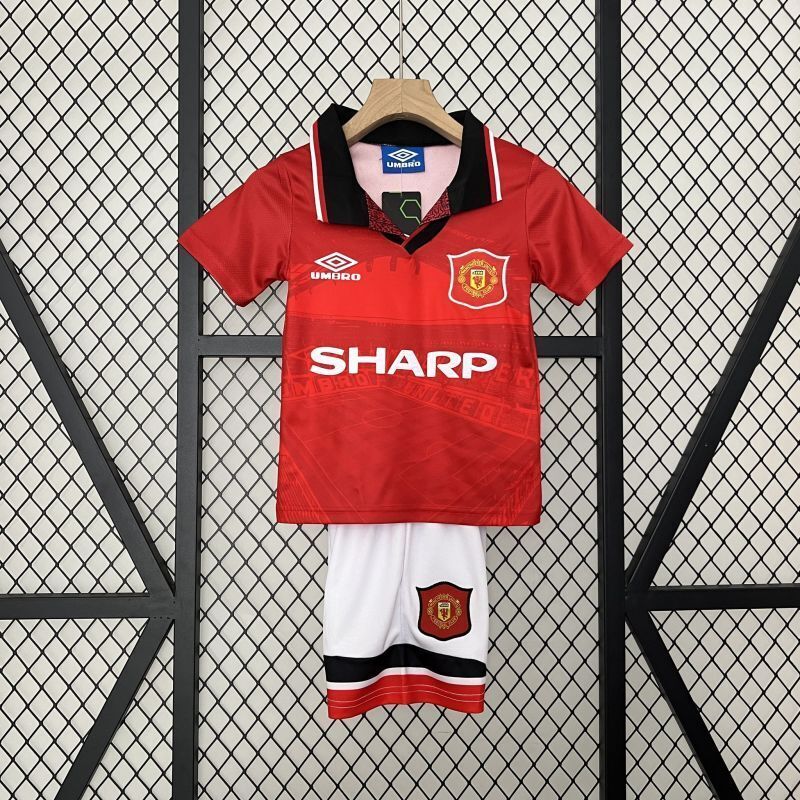 Red kid soccer kit with black collar trim, Manchester United crest, and white shorts