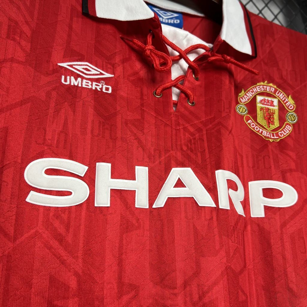 Red football jersey close-up with Umbro logo, red laced neckline, and Manchester United crest