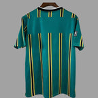 A green short-sleeve soccer jersey with vertical yellow and black stripes, hanging on a wooden hanger against a solid gray background.