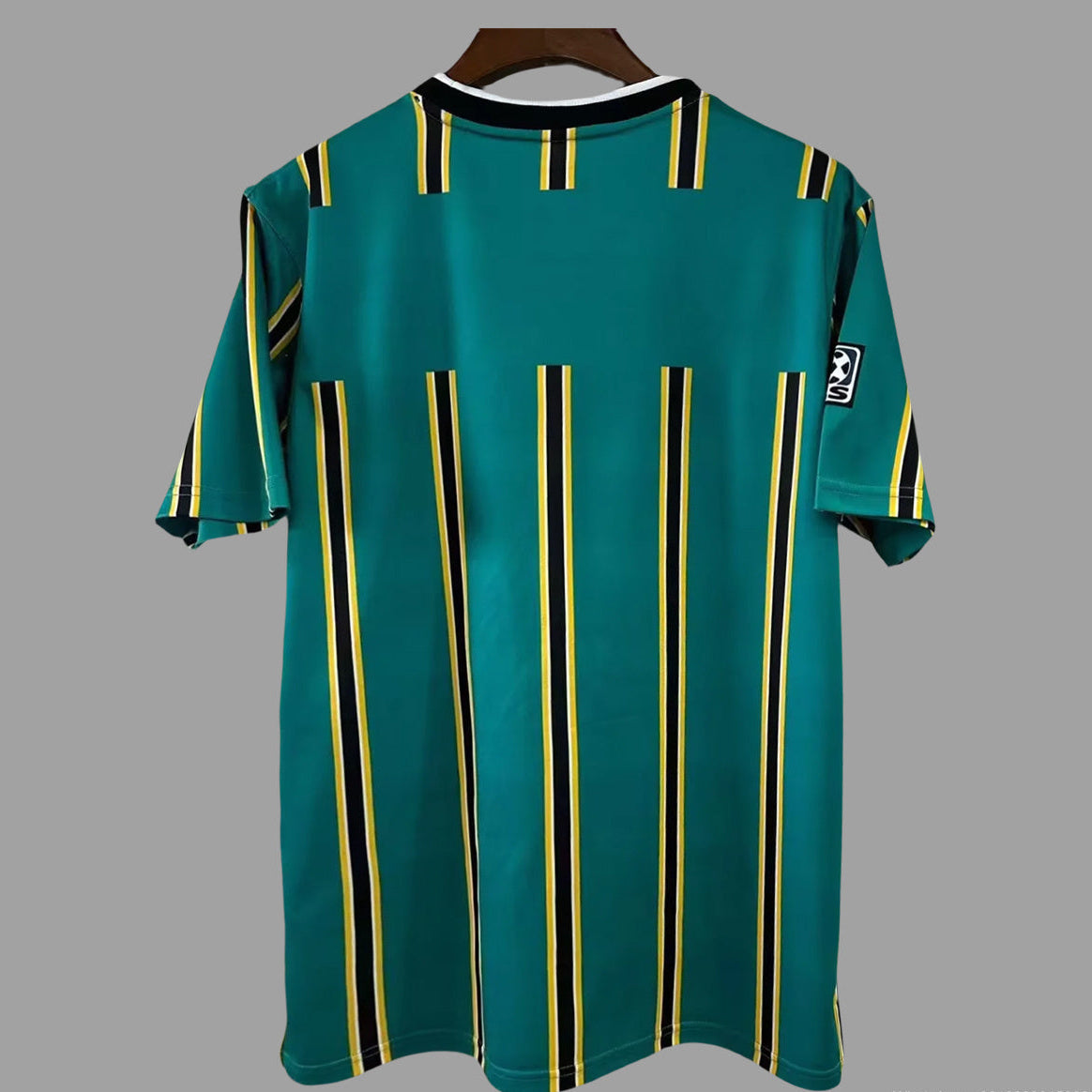 A green short-sleeve soccer jersey with vertical yellow and black stripes, hanging on a wooden hanger against a solid gray background.