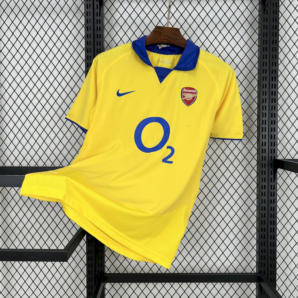 Yellow retro football jersey with blue collar, Arsenal crest, and O2 sponsor print