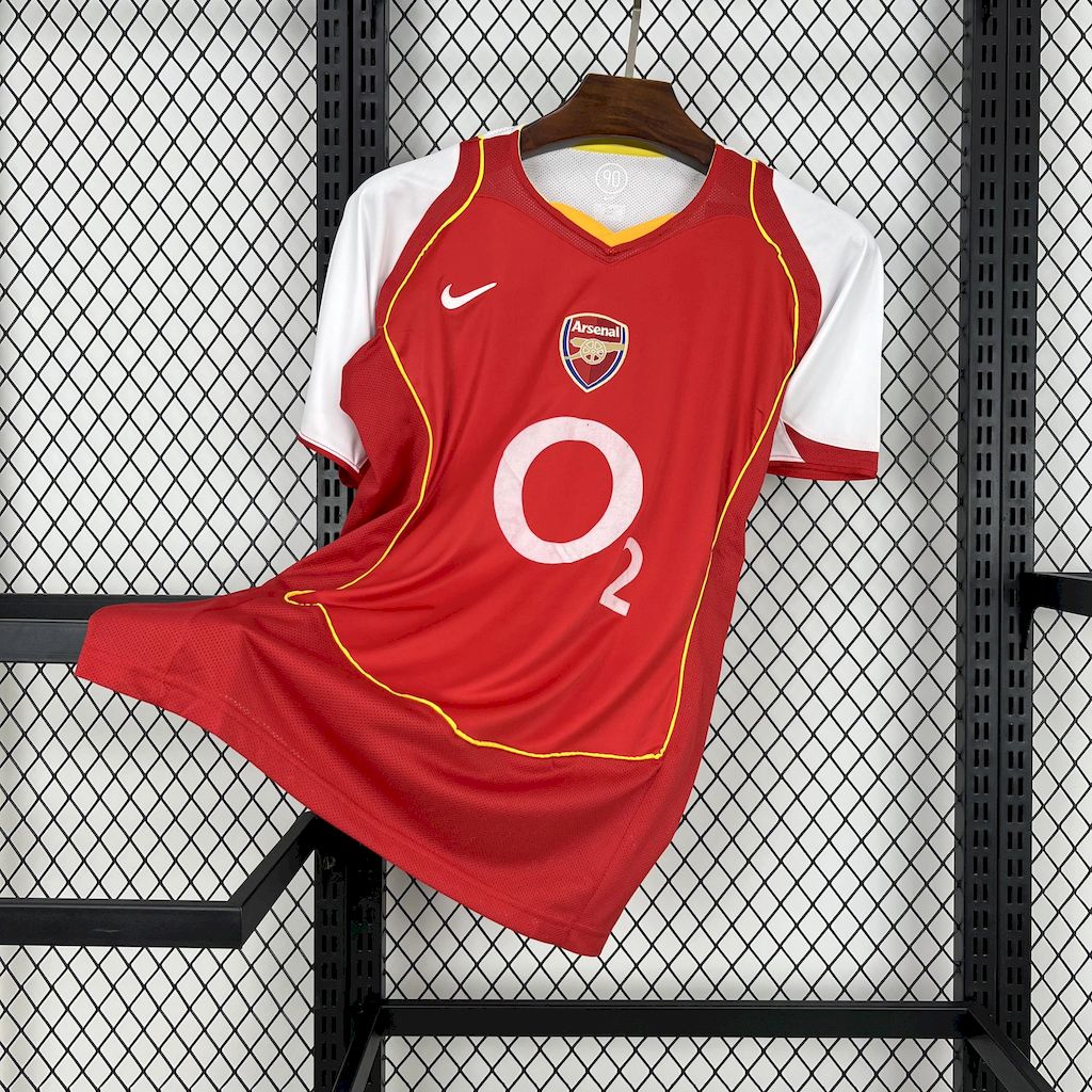 Red soccer jersey with yellow trim, Arsenal crest, Nike swoosh, and 'O2' sponsor