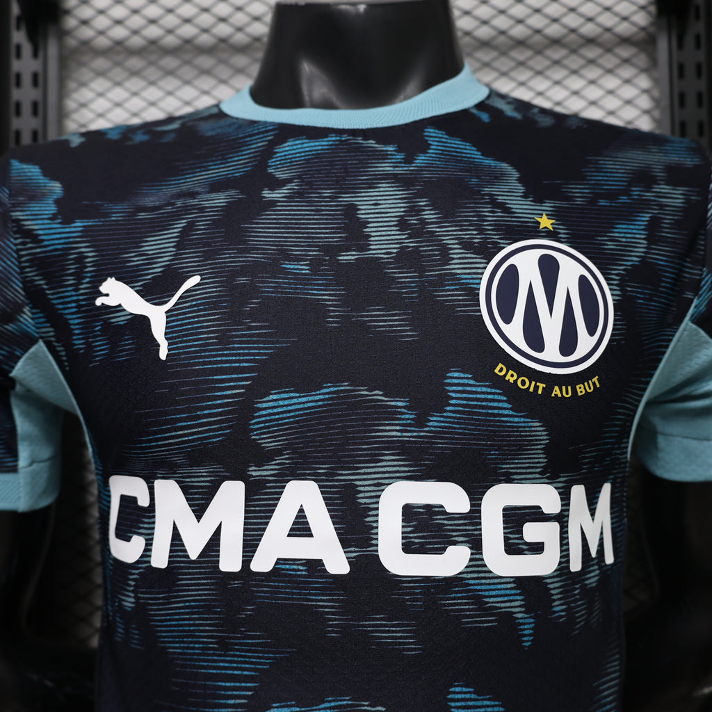 Dark navy soccer jersey with blue camo print, club crest, and 'EMA EGM' sponsor across front.