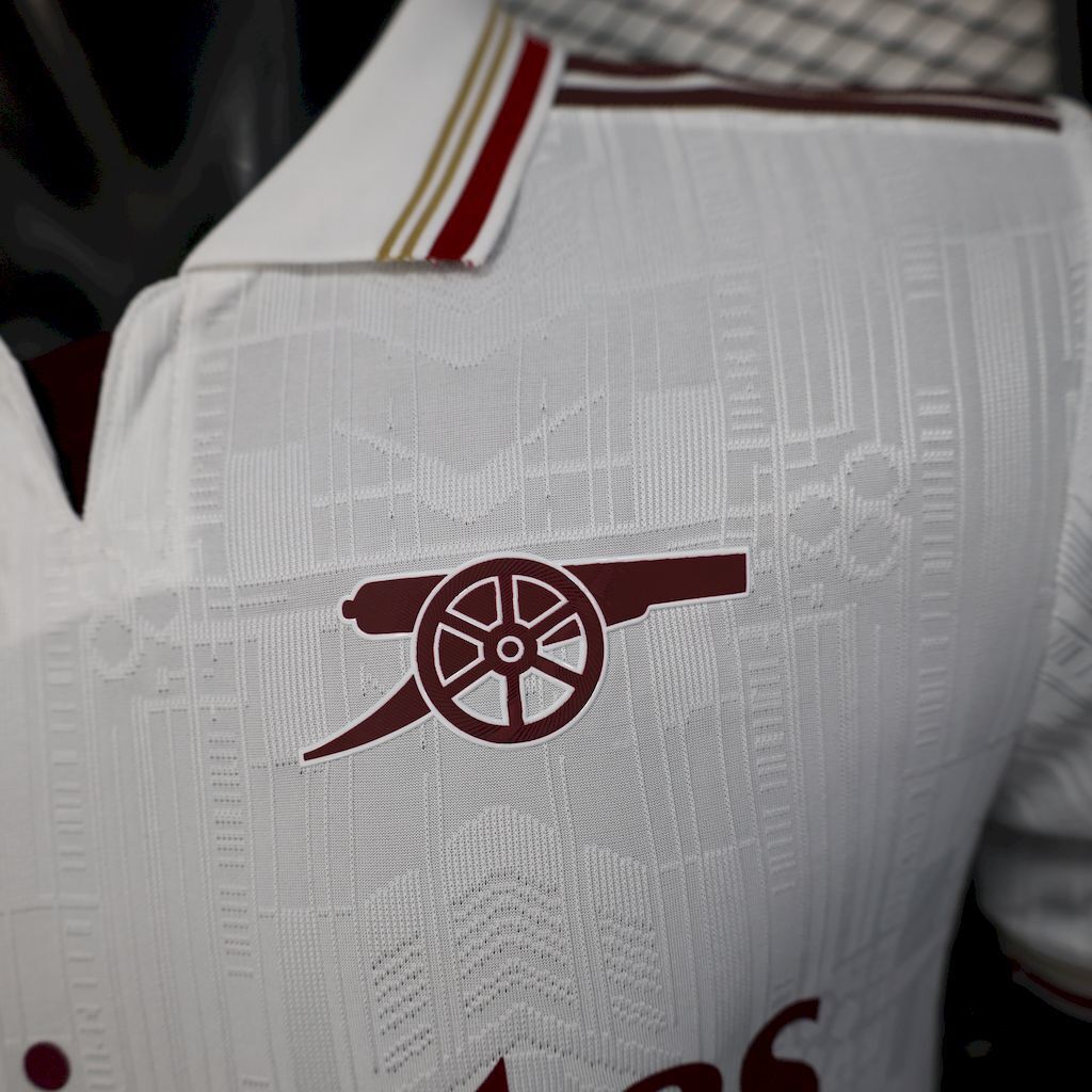 White jersey close-up with maroon emblem and textured geometric pattern, collar trim