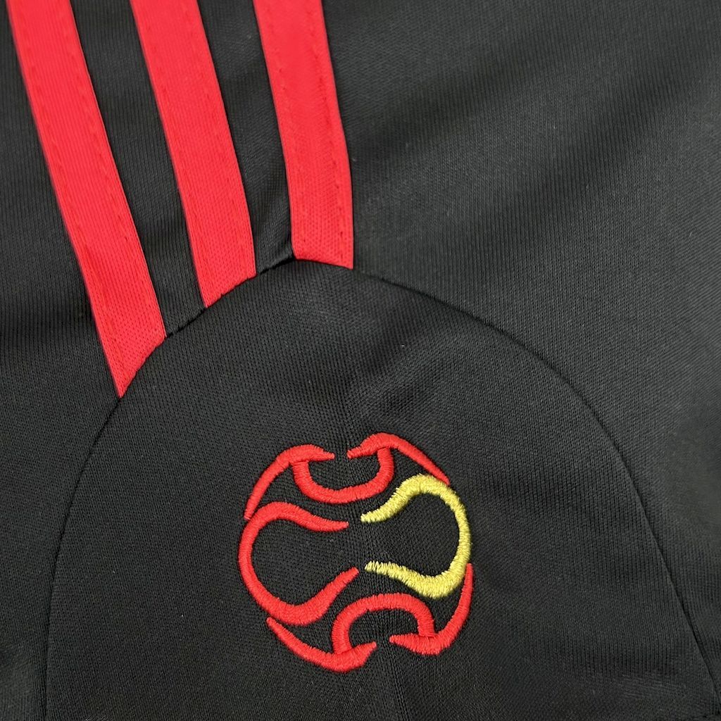 Black jersey shoulder with red three-stripe detail and embroidered crest emblem