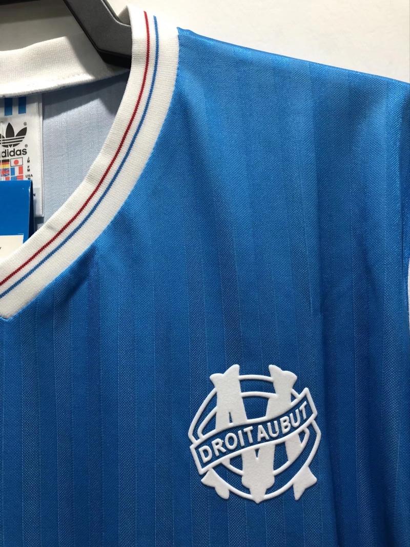 Blue soccer jersey side view with white crest logo and red-blue collar stripes