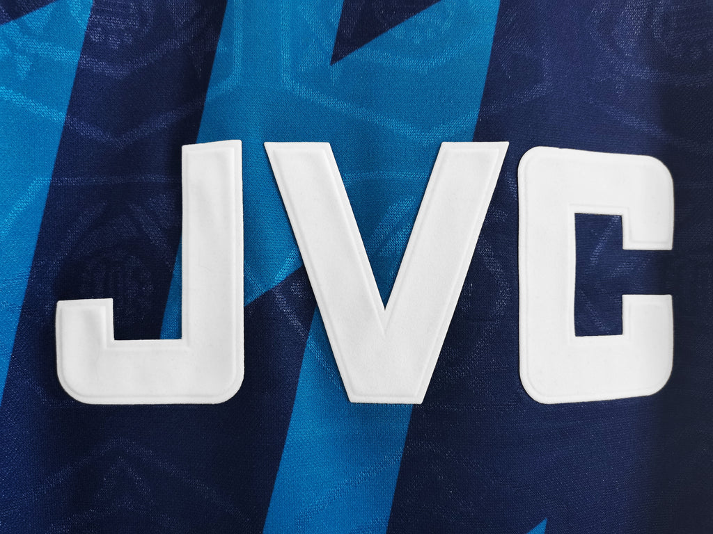Retro football jersey detail, large white 'JVC' letters on blue background
