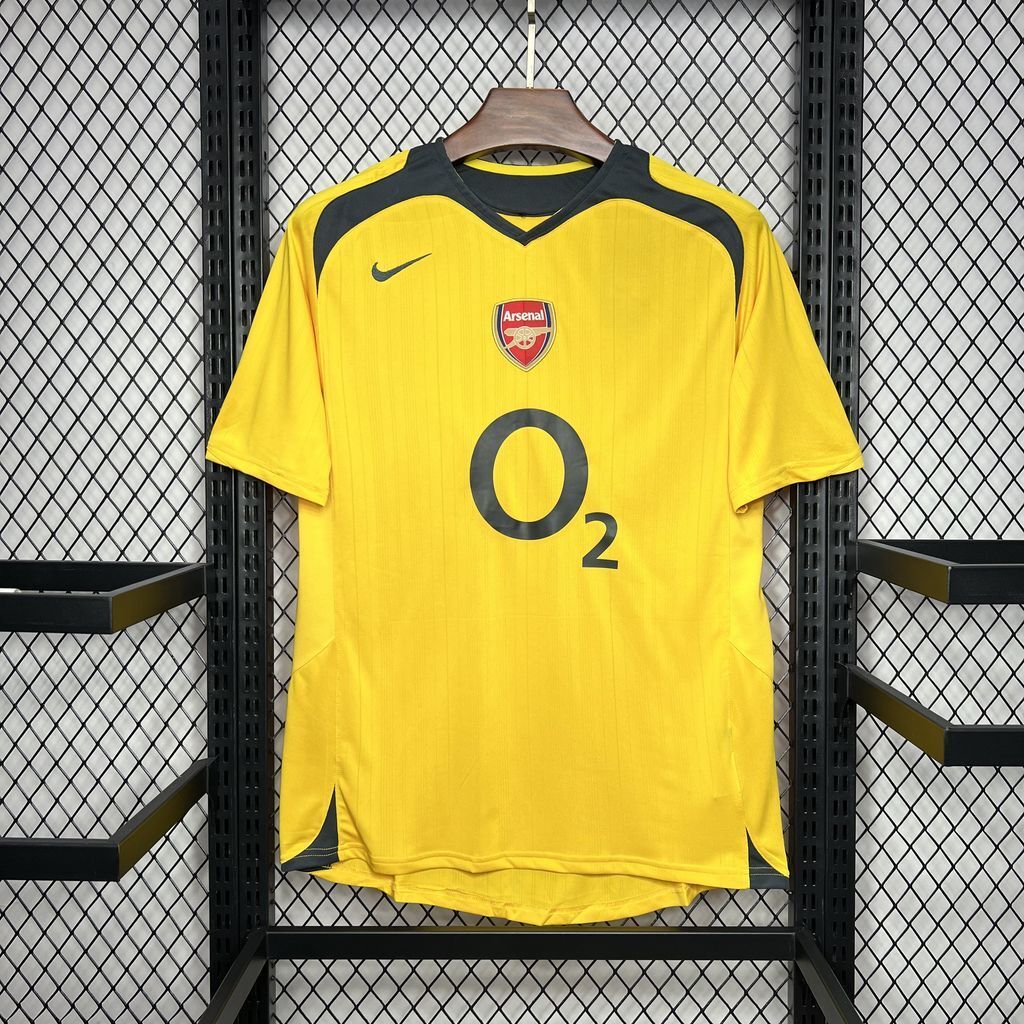 Yellow Arsenal away football jersey on hanger with crest, Nike swoosh, and O2 sponsor