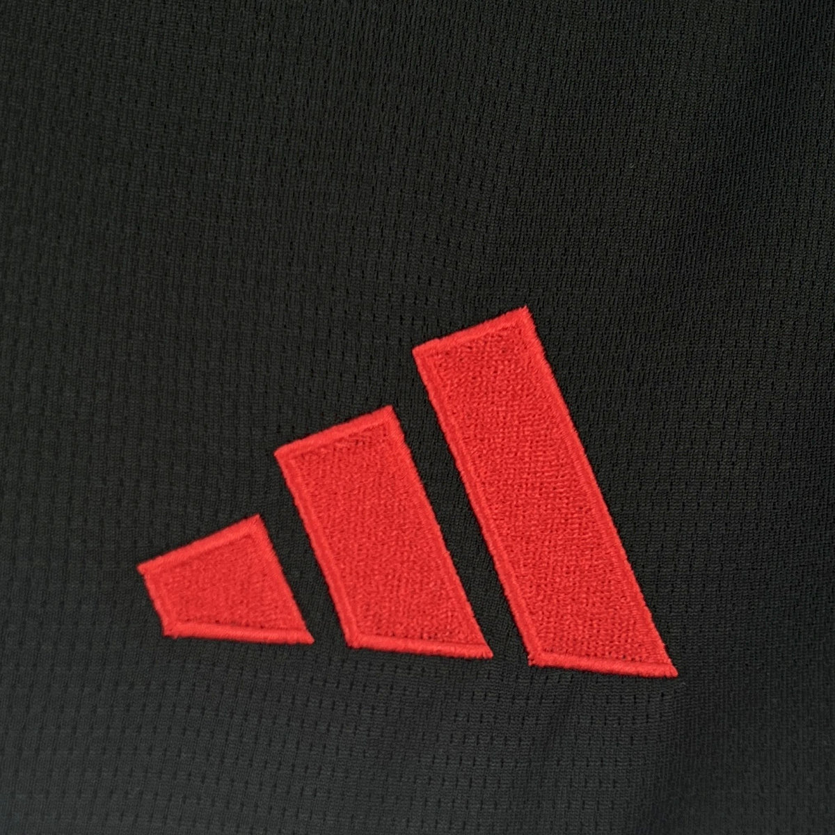 Red Adidas triple-stripe logo on black football jersey