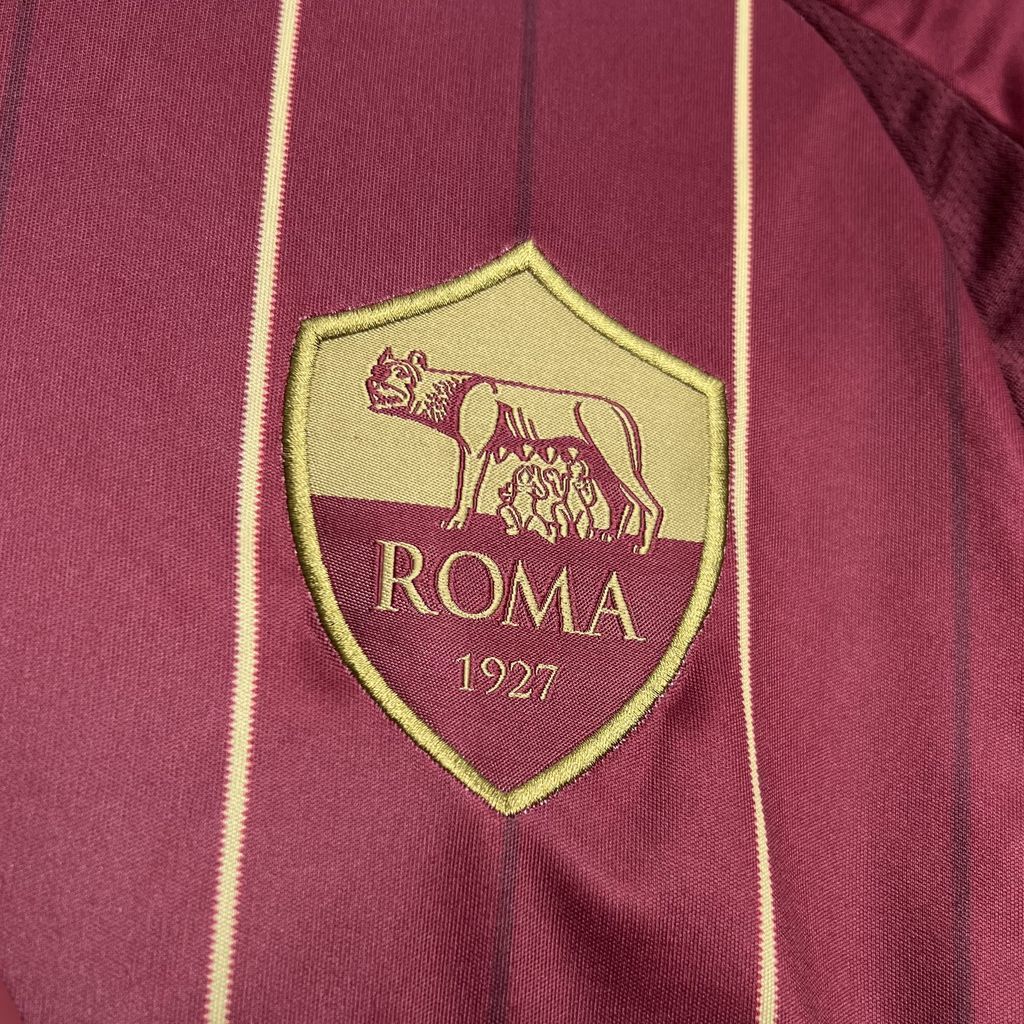 Roma crest patch on burgundy jersey with gold outline and vertical stripe accents