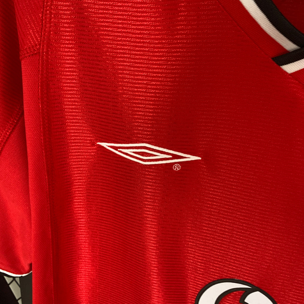Red football shirt close-up of Umbro-style chest logo with white sleeve trim