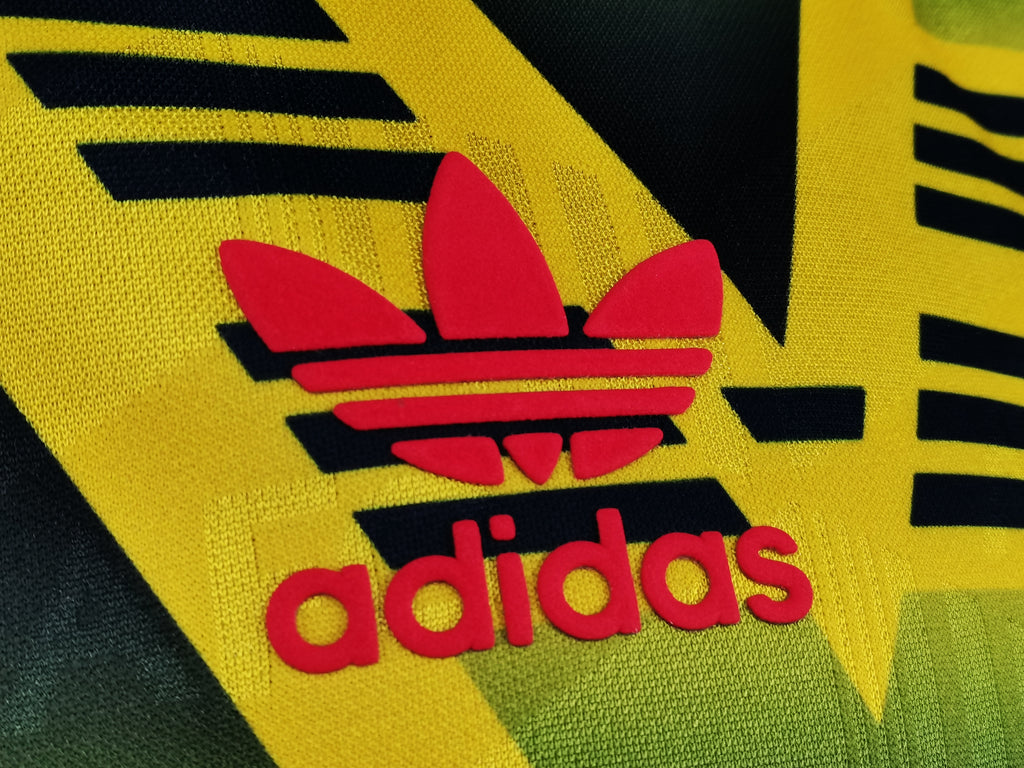 Yellow jersey detail with black outline Adidas trefoil and red adidas text