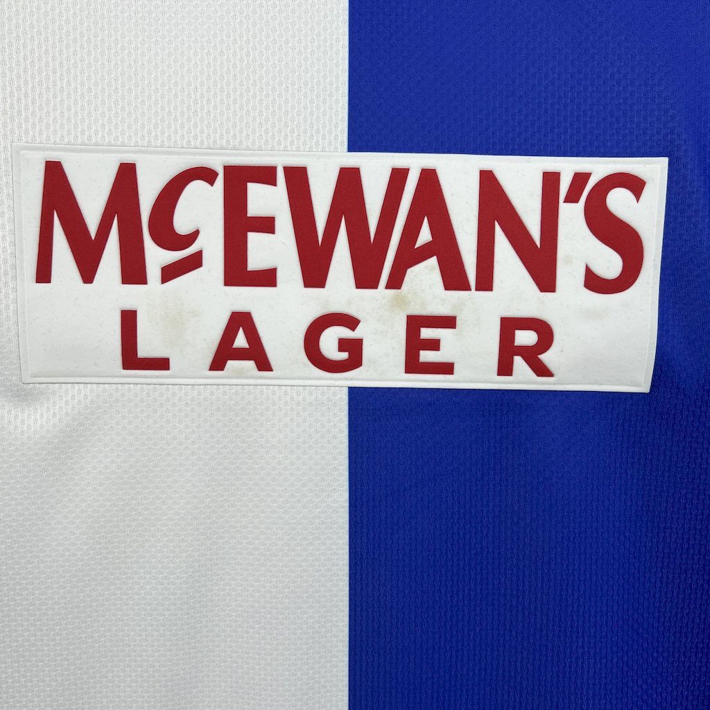 Close-up of McEwan’s Lager sponsor patch on white panel of retro home shirt