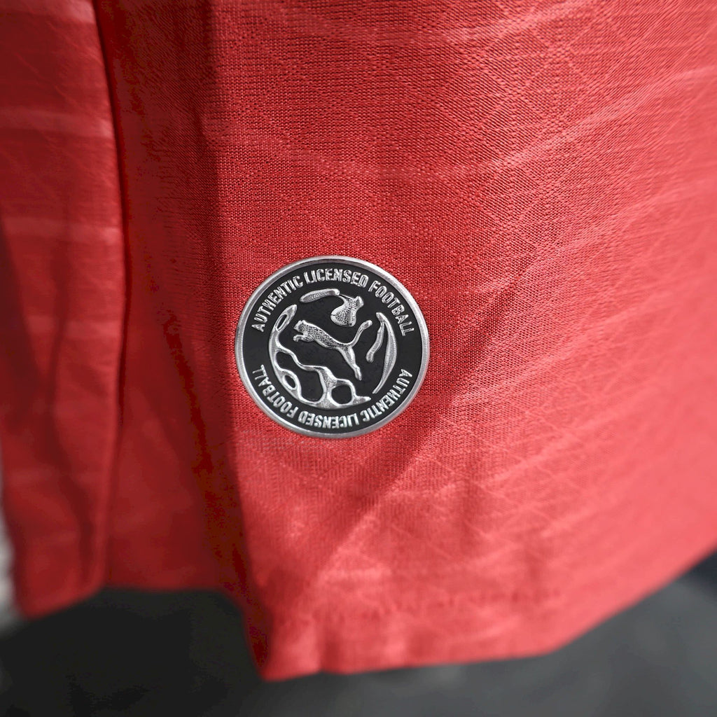 Red soccer jersey patch with Puma authentication stamp near lower front