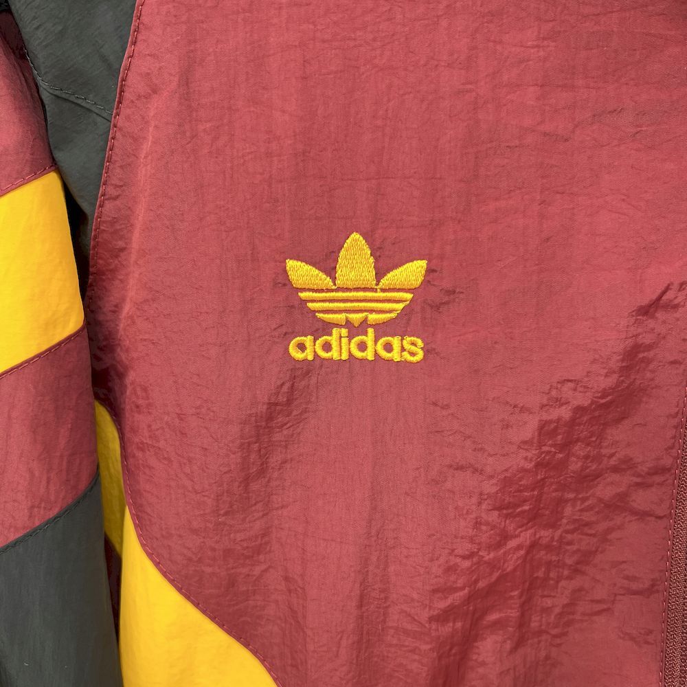 Maroon windbreaker chest with gold adidas trefoil logo, zip seam visible, side panel.