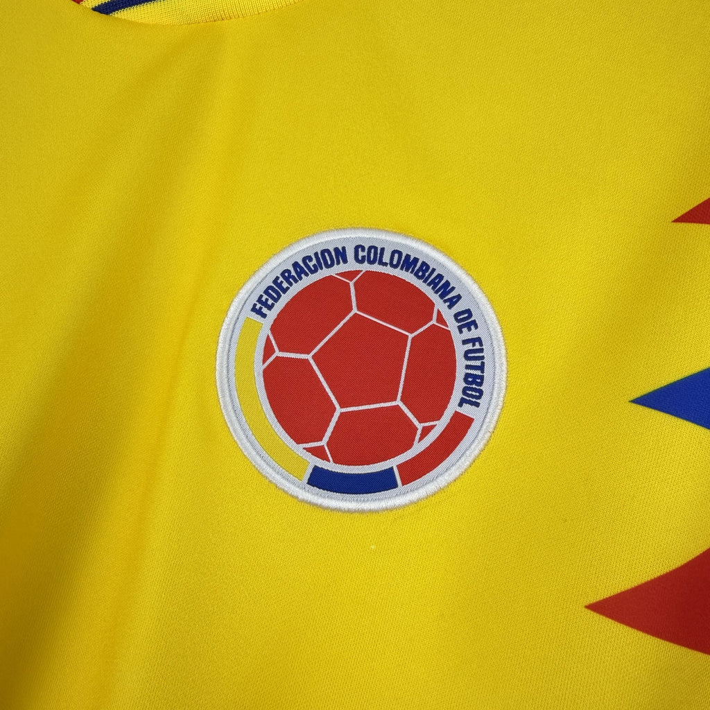 Colombia federation football crest on yellow jersey, circular red-and-blue soccer ball badge