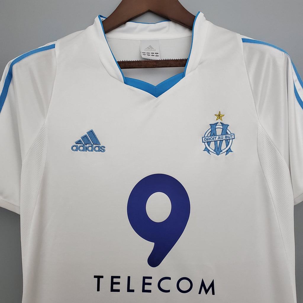 White football jersey with blue V-neck, adidas mark, and Marseille crest