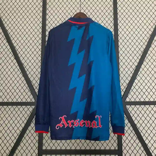 Retro soccer jersey back with Arsenal lettering and lightning graphic, blue and navy long sleeves.