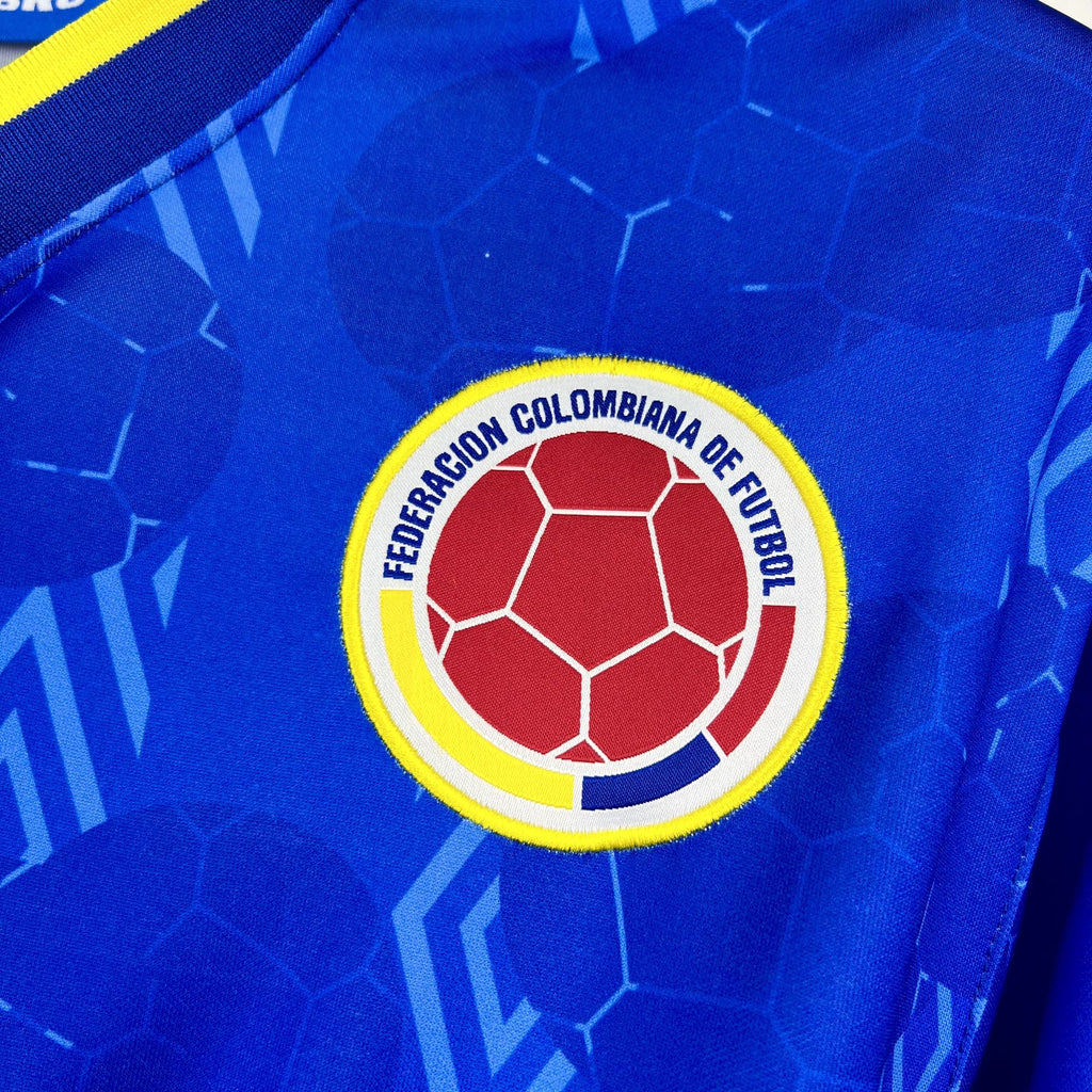 Colombian football federation crest on blue jersey, circular logo with yellow border