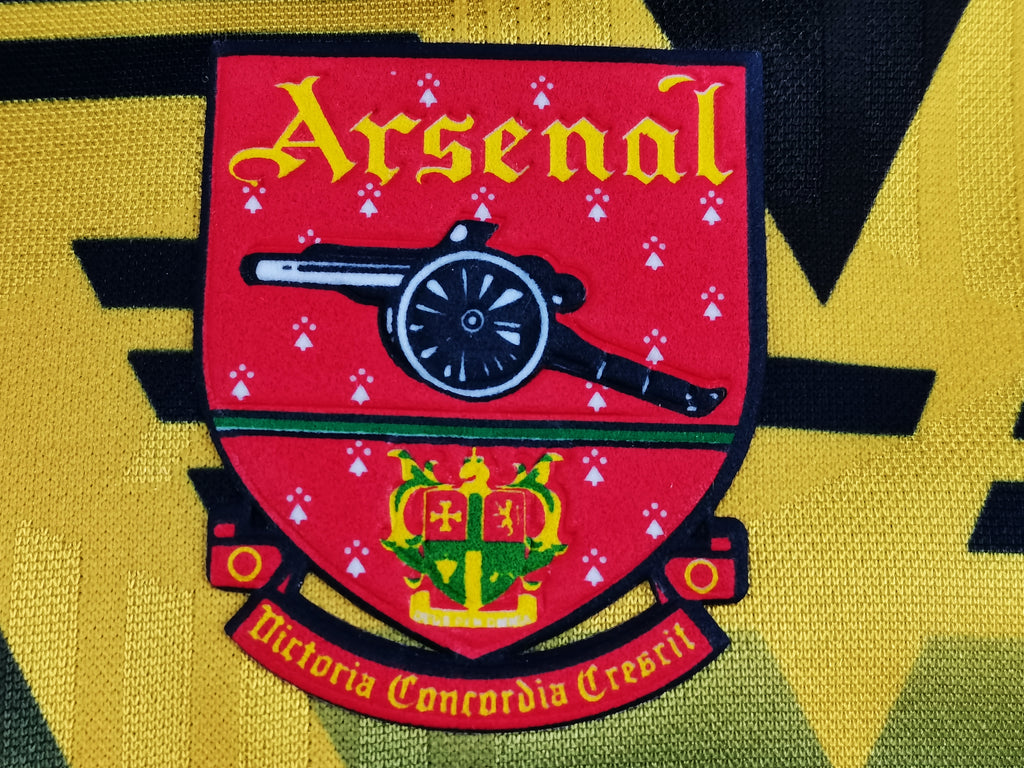 Yellow jersey crest with Arsenal cannon emblem, crown, and red banner
