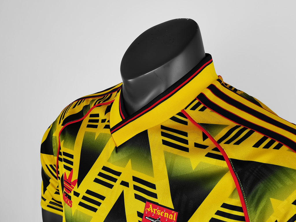 Yellow football jersey collar with red-and-black trim and small Arsenal crest