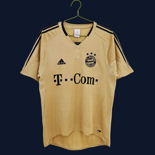 Gold Bayern Munich retro football jersey with adidas logo, T‑Com sponsor, team crest.