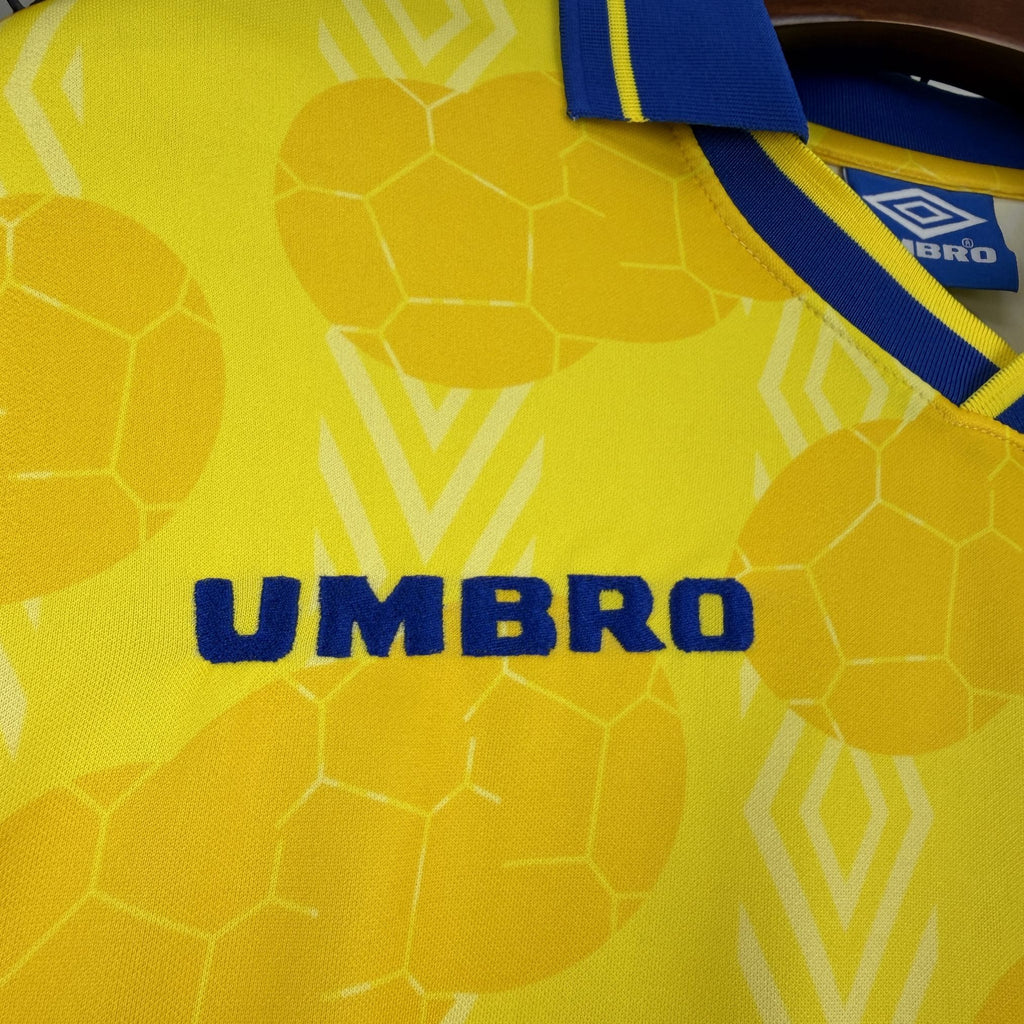 UMBRO logo on yellow soccer jersey with geometric pattern and blue collar edge.