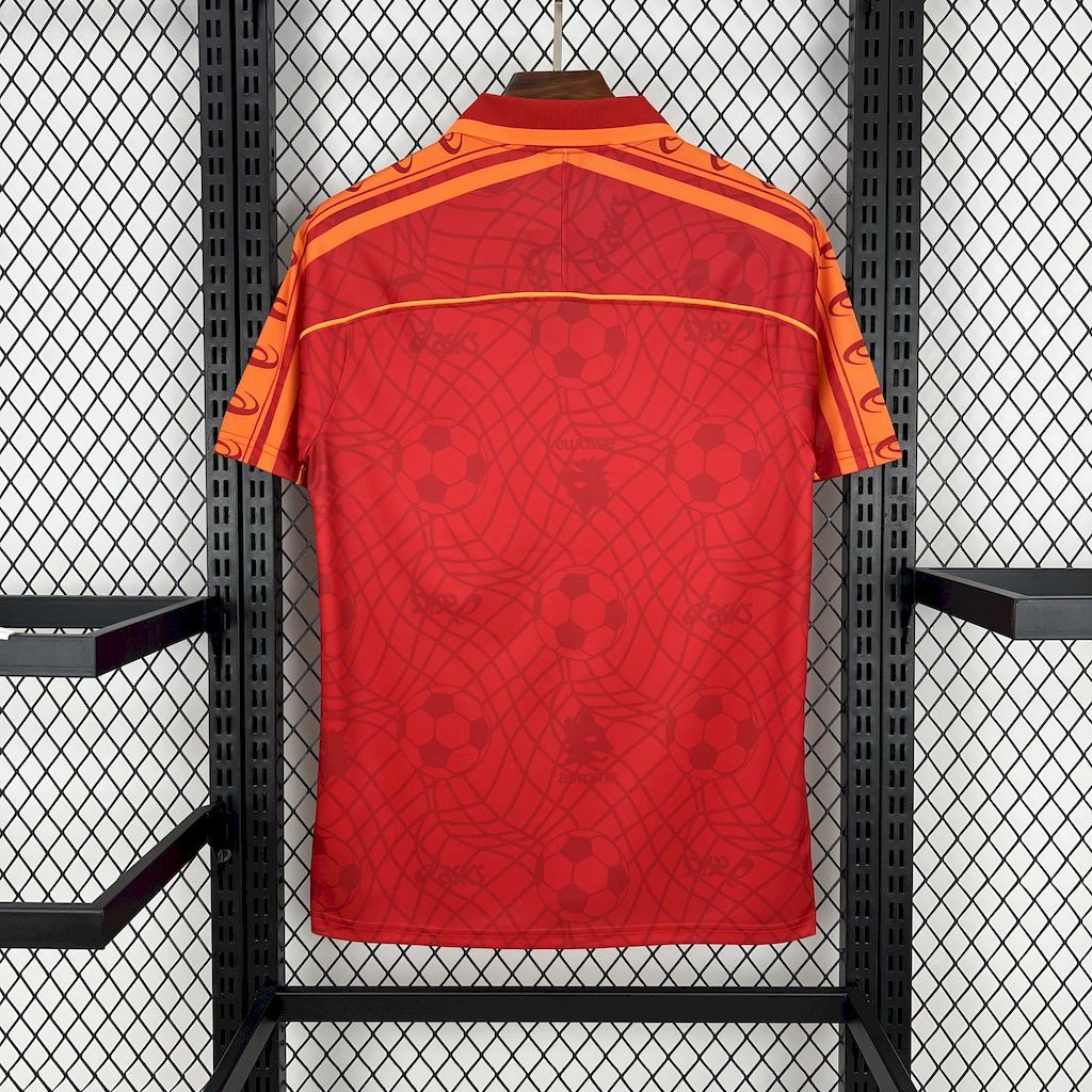 Red soccer home jersey with orange trim, patterned back view.
