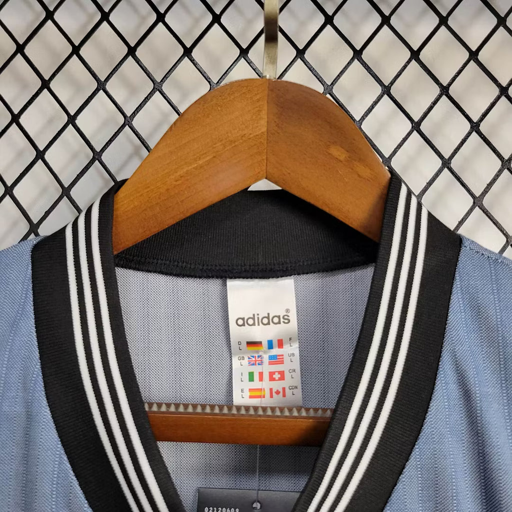 Adidas logo and V-neck trim inside light blue retro football jersey on wooden hanger