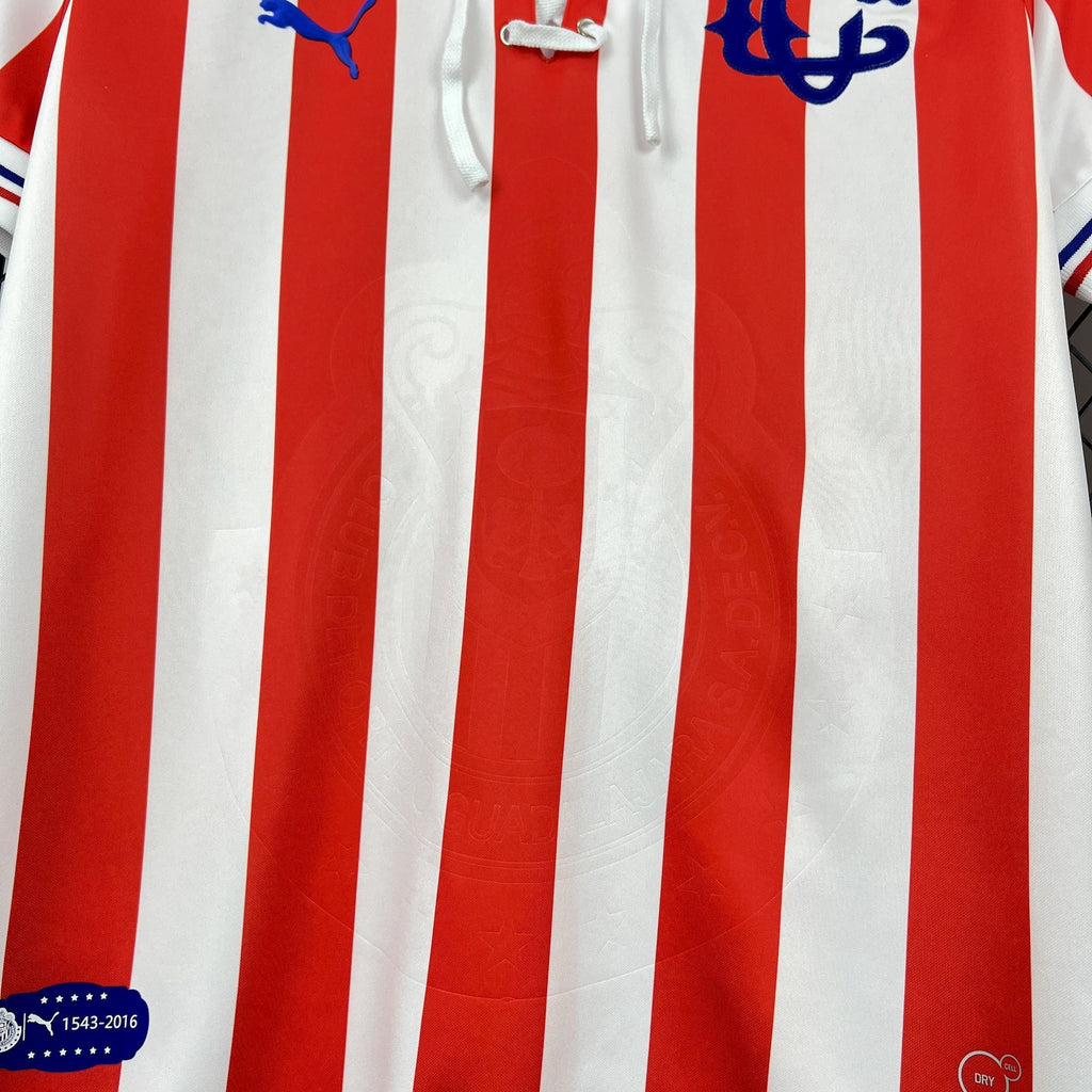 Retro soccer jersey close-up of red-and-white vertical stripes with blue emblem accents.