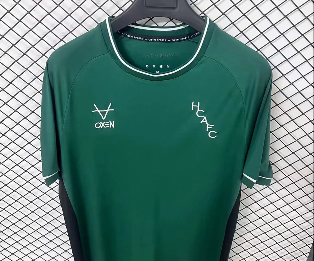 Green goalkeeper fan jersey front close-up with white neck trim, OXEN and HCAF FC logos