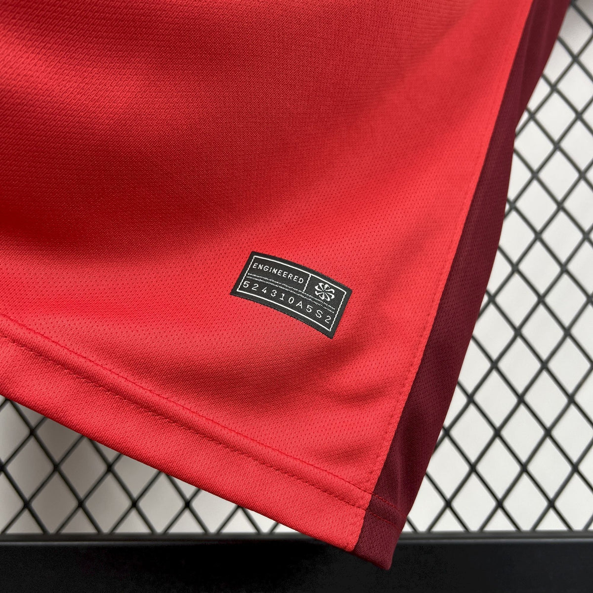 Red soccer jersey hem with small black size tag near side seam.