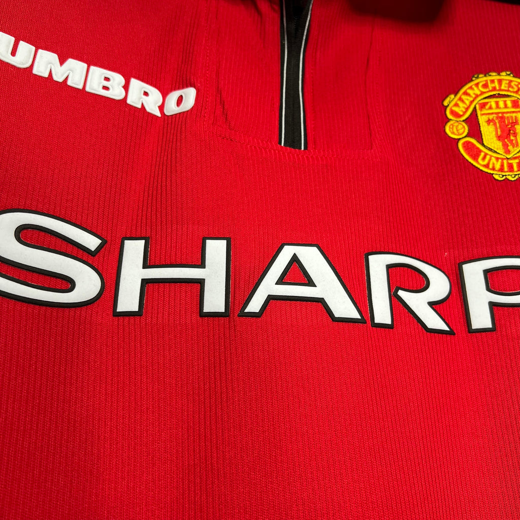 Red jersey close-up showing SHARP sponsor print and club crest on the chest