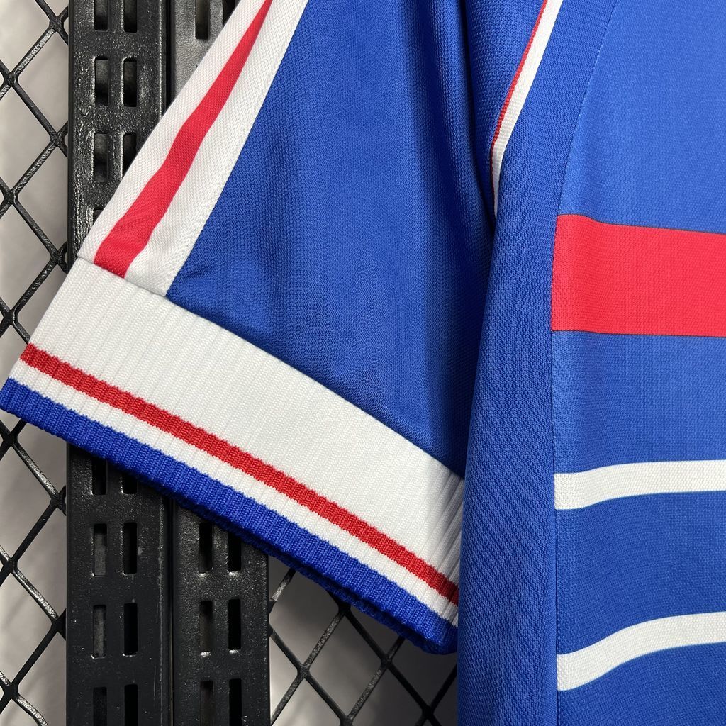 Blue football jersey sleeve and hem detail with white stripes and red accent band.