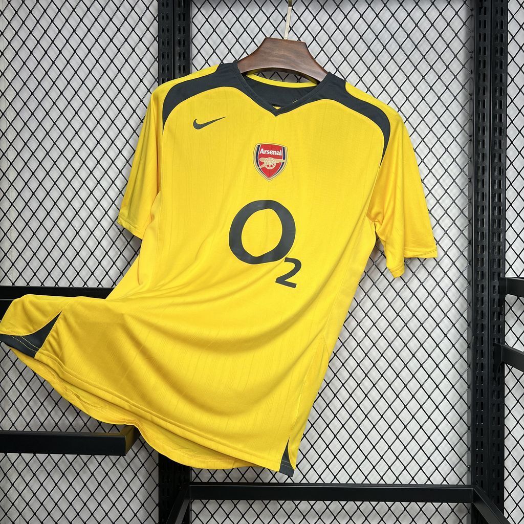Yellow Arsenal away football jersey with dark trim, crest on chest, and O2 sponsor logo